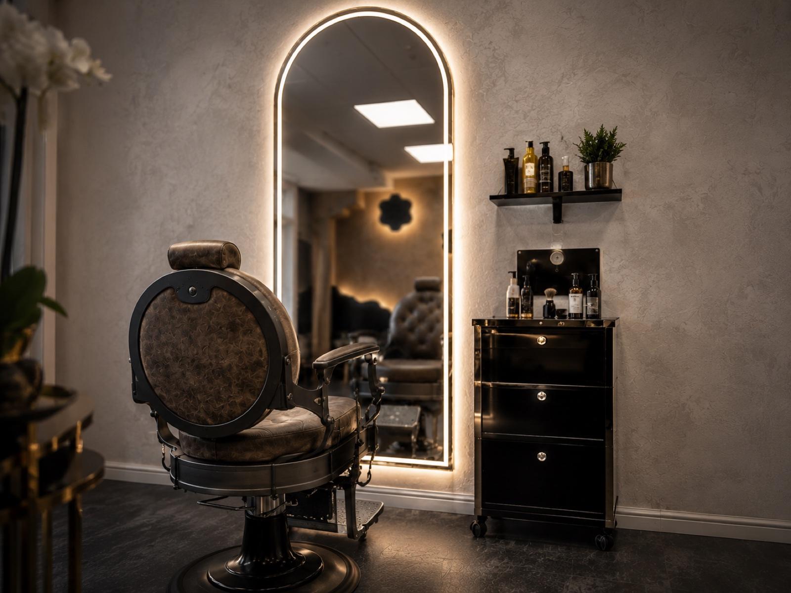 A vintage barber chair beside an arched, backlit mirror and grooming products at Empire salon in Corby